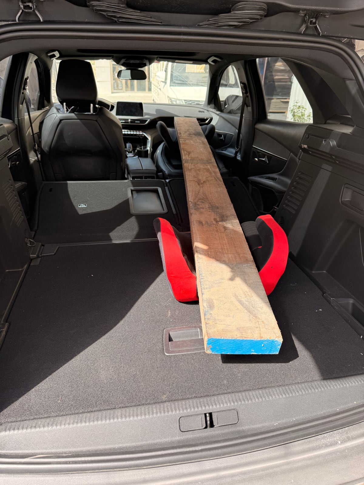 A rough board resting on a red child booster seat in the back of a car