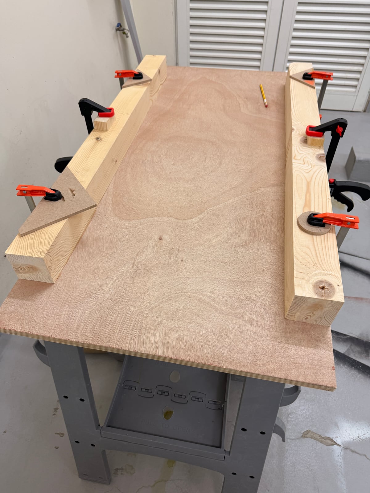 Two 4x4 rails clamped along the edges of a plywood sheet on sawhorses
