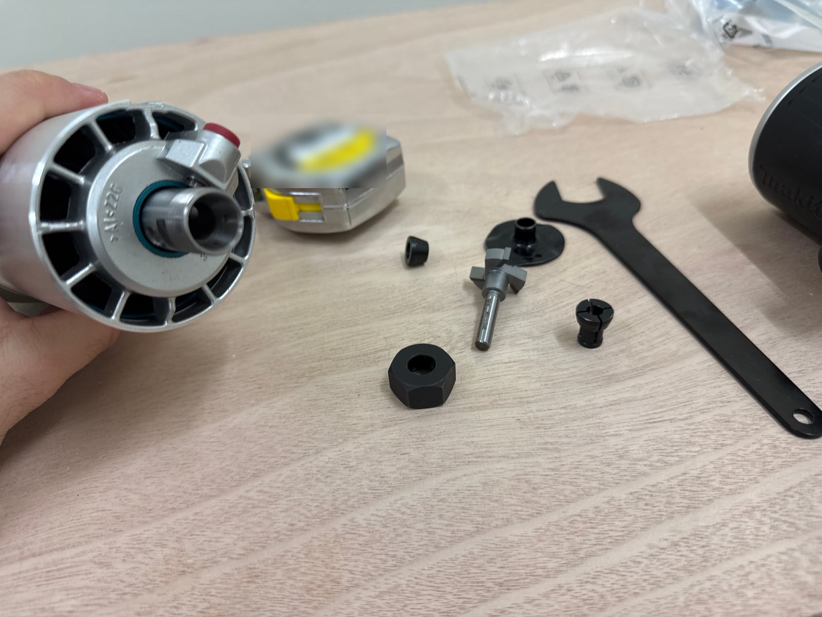 A router motor, collets, a collet nut, a wrench, the surfacing bit and a tape measure laid out on plywood