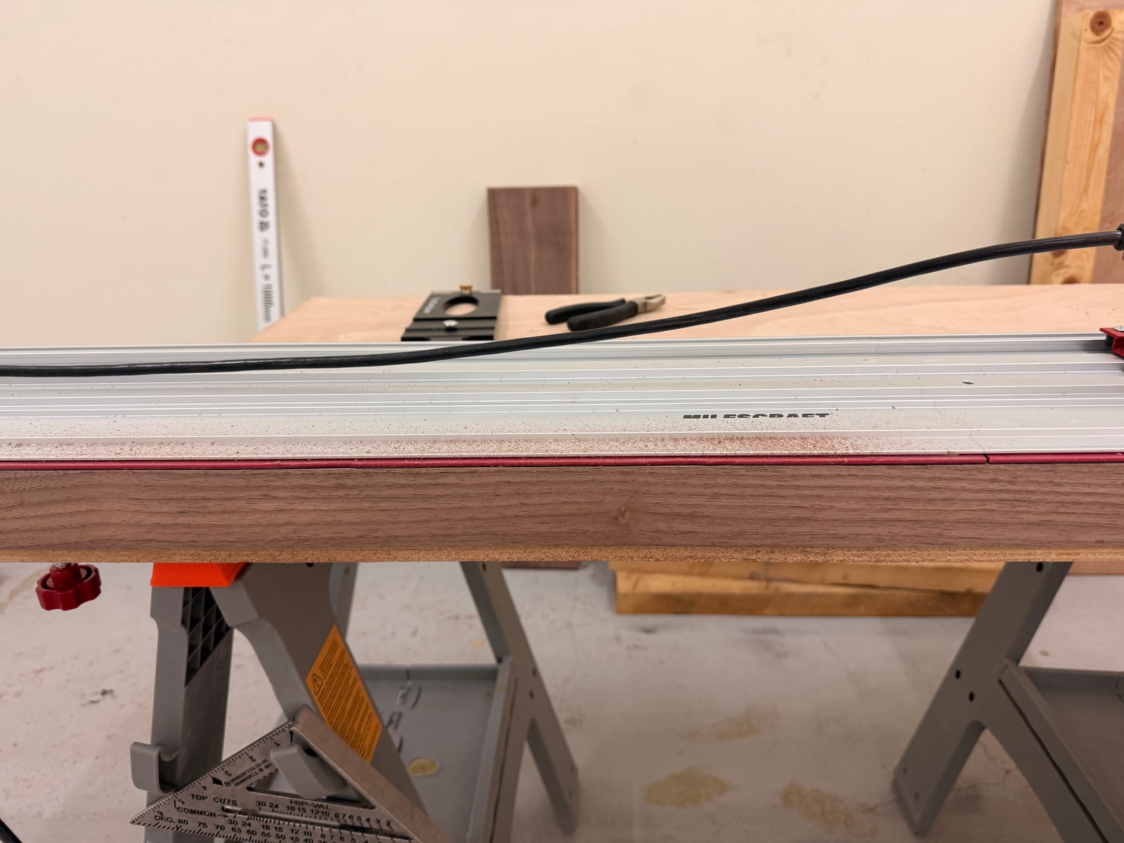 A Milescraft aluminium saw track lying along a walnut board on sawhorses
