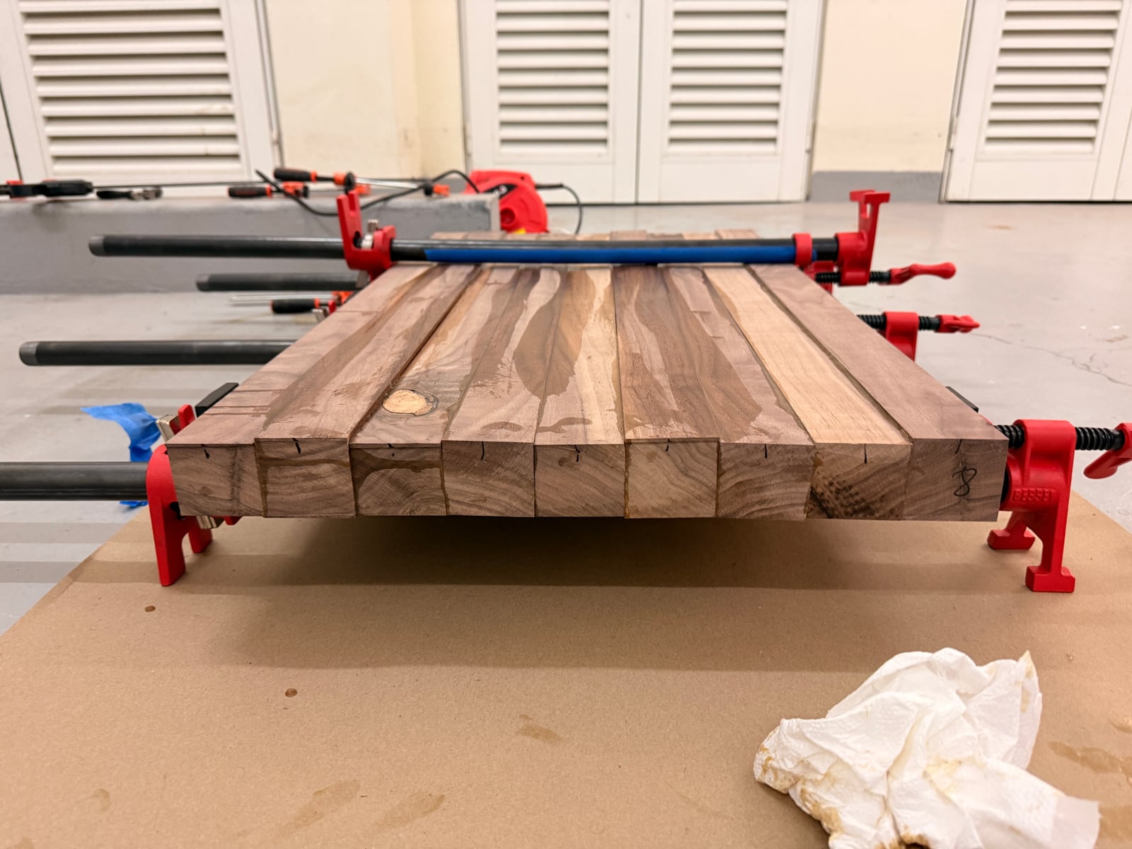 Walnut strips glued up in red pipe clamps, their ends visibly uneven