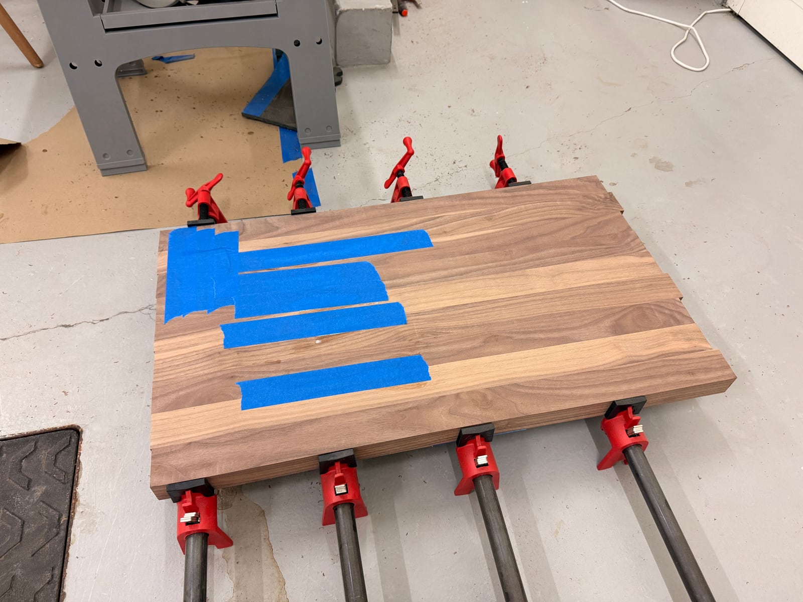 The walnut panel back in the pipe clamps, with blue tape along one joint