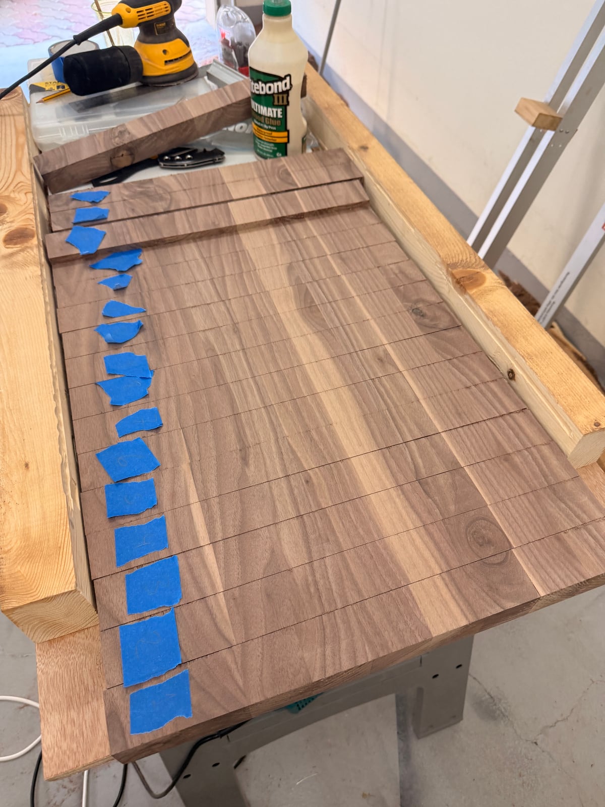 Walnut strips laid side by side on the sled, blue tape labels along one end, with a bottle of Titebond nearby