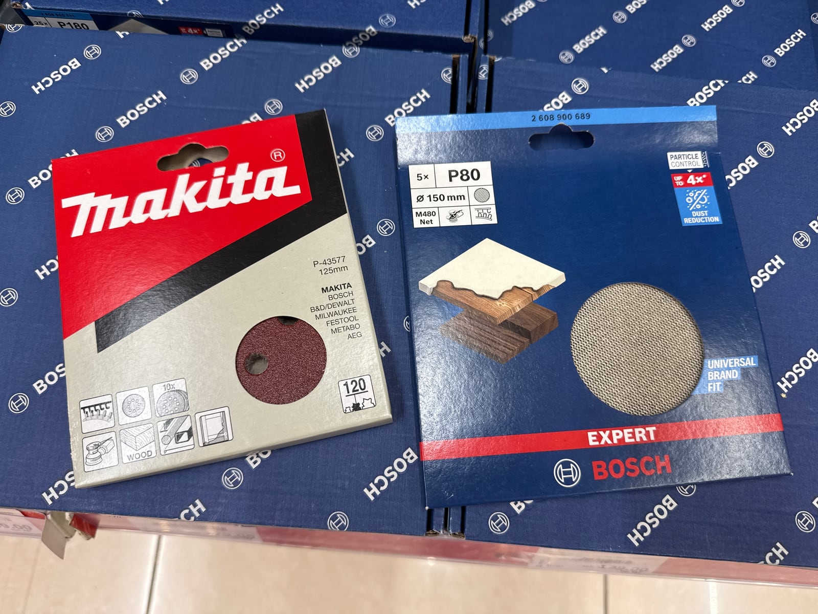 A pack of Makita 125mm sanding discs next to a pack of Bosch M480 net discs