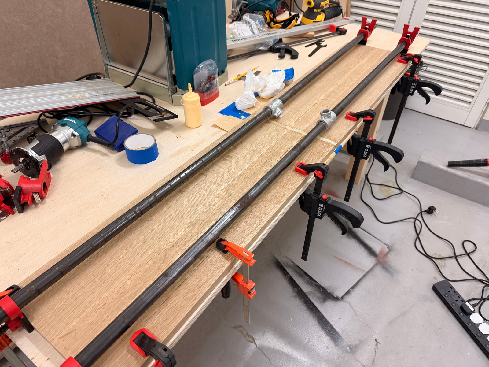 The oak panel in the glue-up, held by two pipe clamps joined end to end into one long clamp