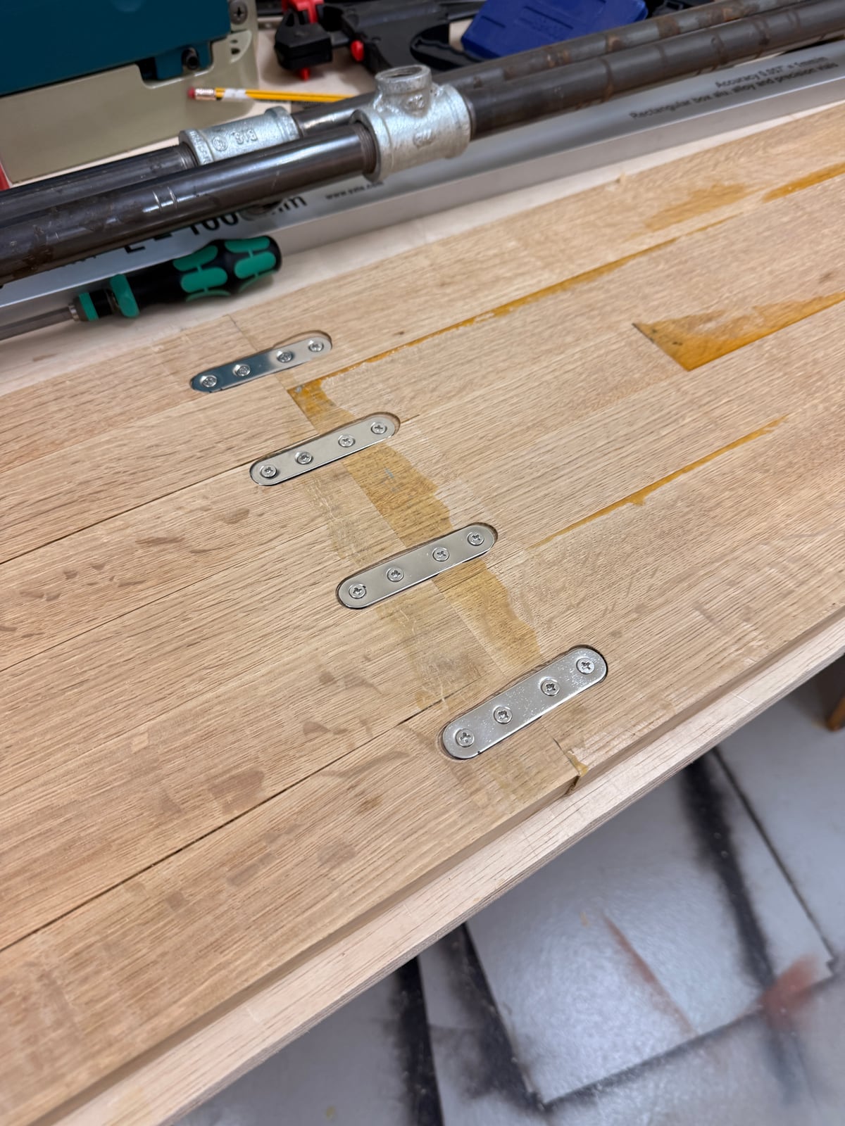 The underside of the oak panel with four metal mending plates recessed across the joint, glue pooled along the seams