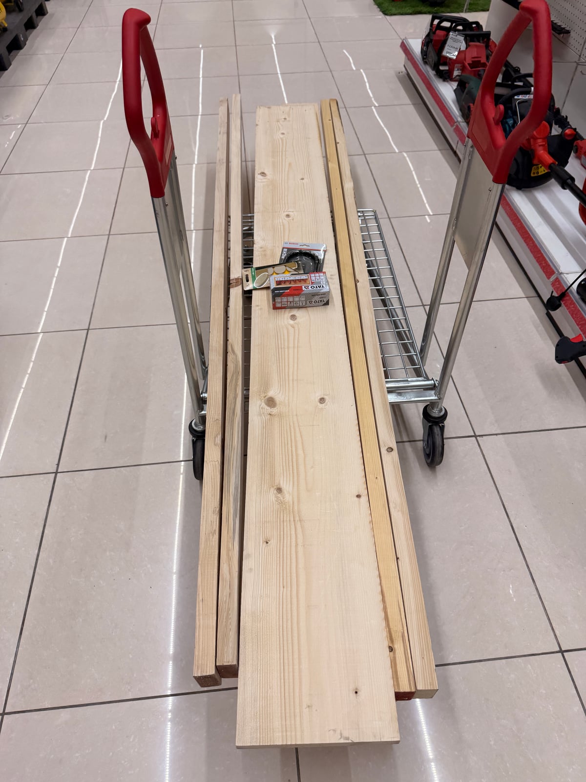 A store trolley loaded with long softwood boards, narrow 2x3s alongside a wide board