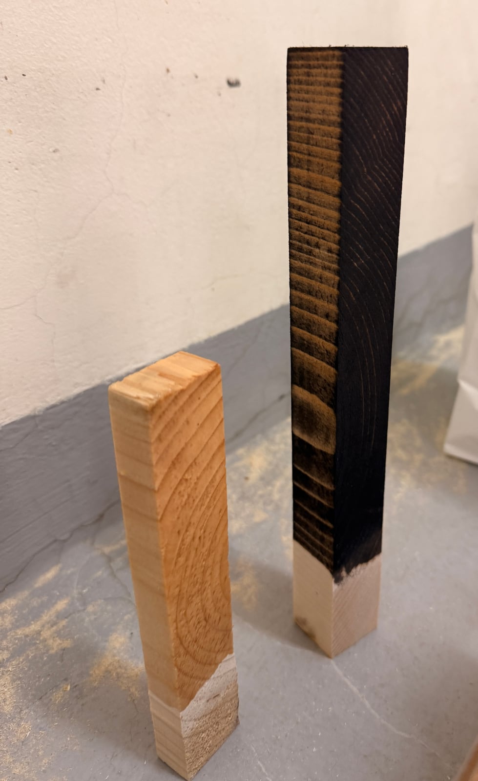 Two short softwood offcuts standing on end, one honey-coloured under clear varnish and one stained dark brown, each with a bare end