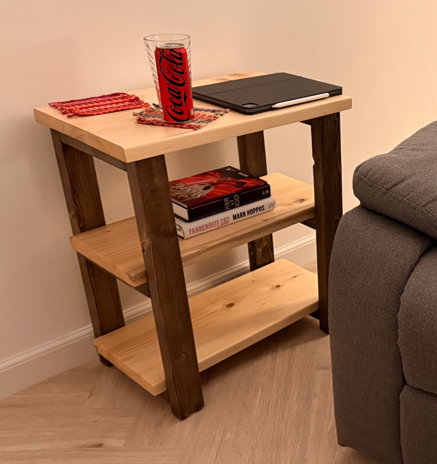 The finished side table beside a grey sofa: dark stained legs, a natural glued-up top and two natural shelves, with a can of Coke Zero on top