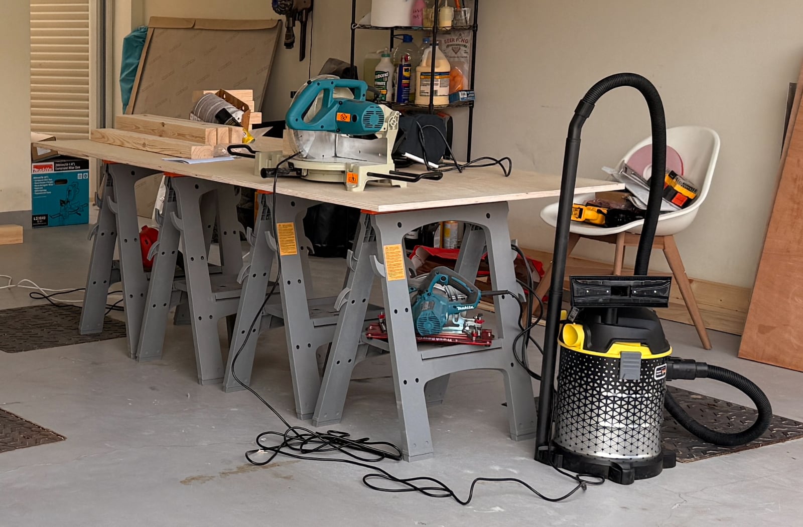 The garage set up for cutting: a board across two sawhorses with the miter saw and shop vac beside it