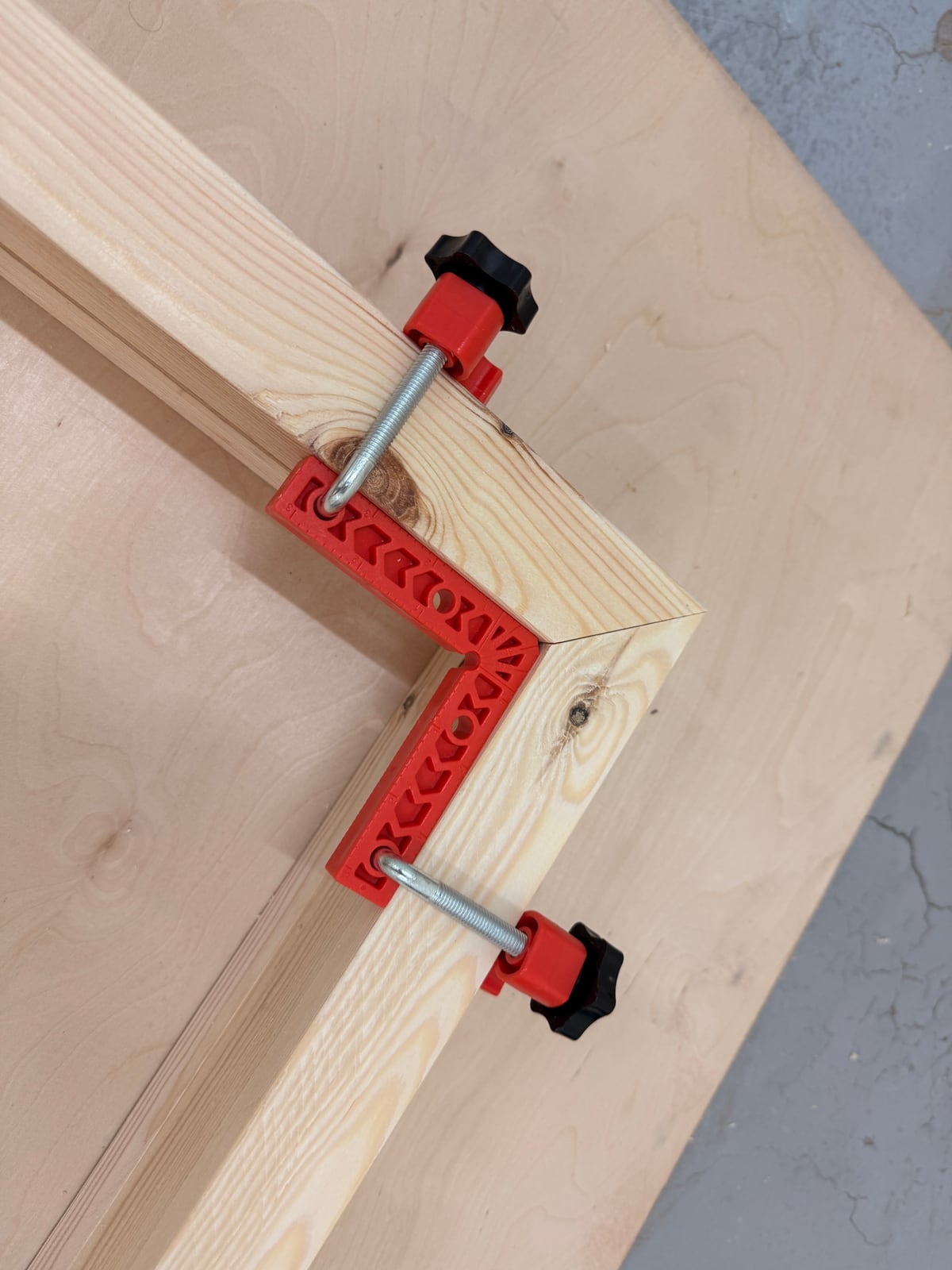 Two red plastic corner clamps holding a mitered 2x4 corner square