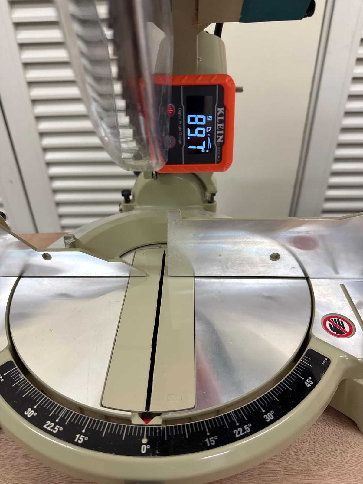 A digital angle gauge stuck to a miter saw blade, reading 89.7 degrees
