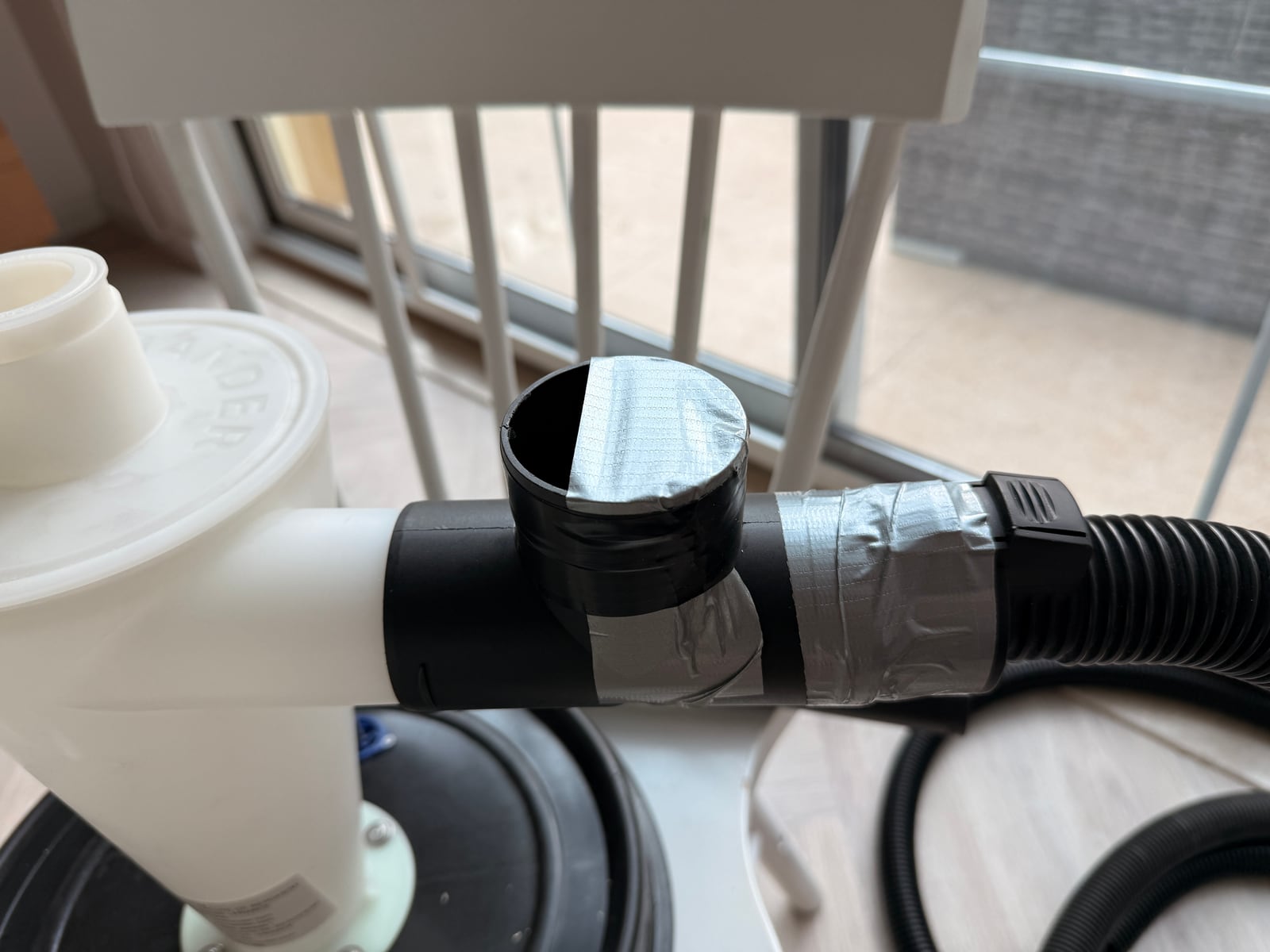 A T-shaped dust hose adapter with tape covering the open branch