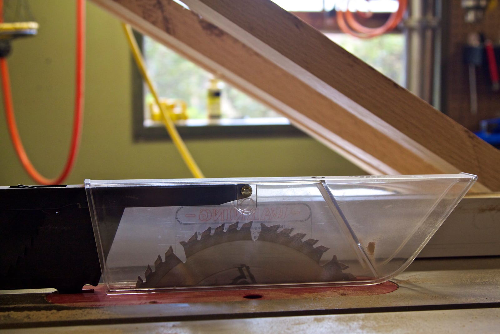 A clear guard sitting over a table saw blade -- it keeps hands out of the blade path without hiding the cut line.