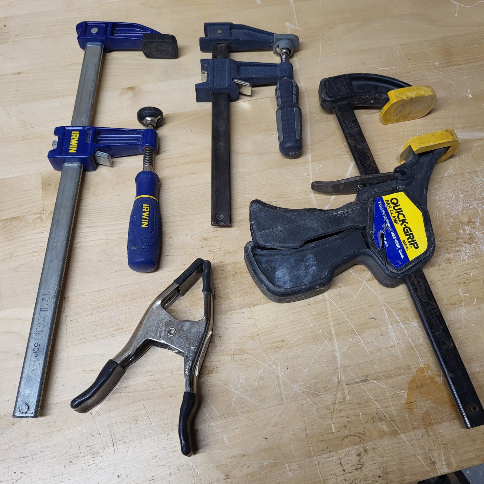 F-clamps in two sizes, with a trigger clamp and a spring clamp alongside. The sliding lower jaw is what lets an F-clamp take any width up to its bar length.