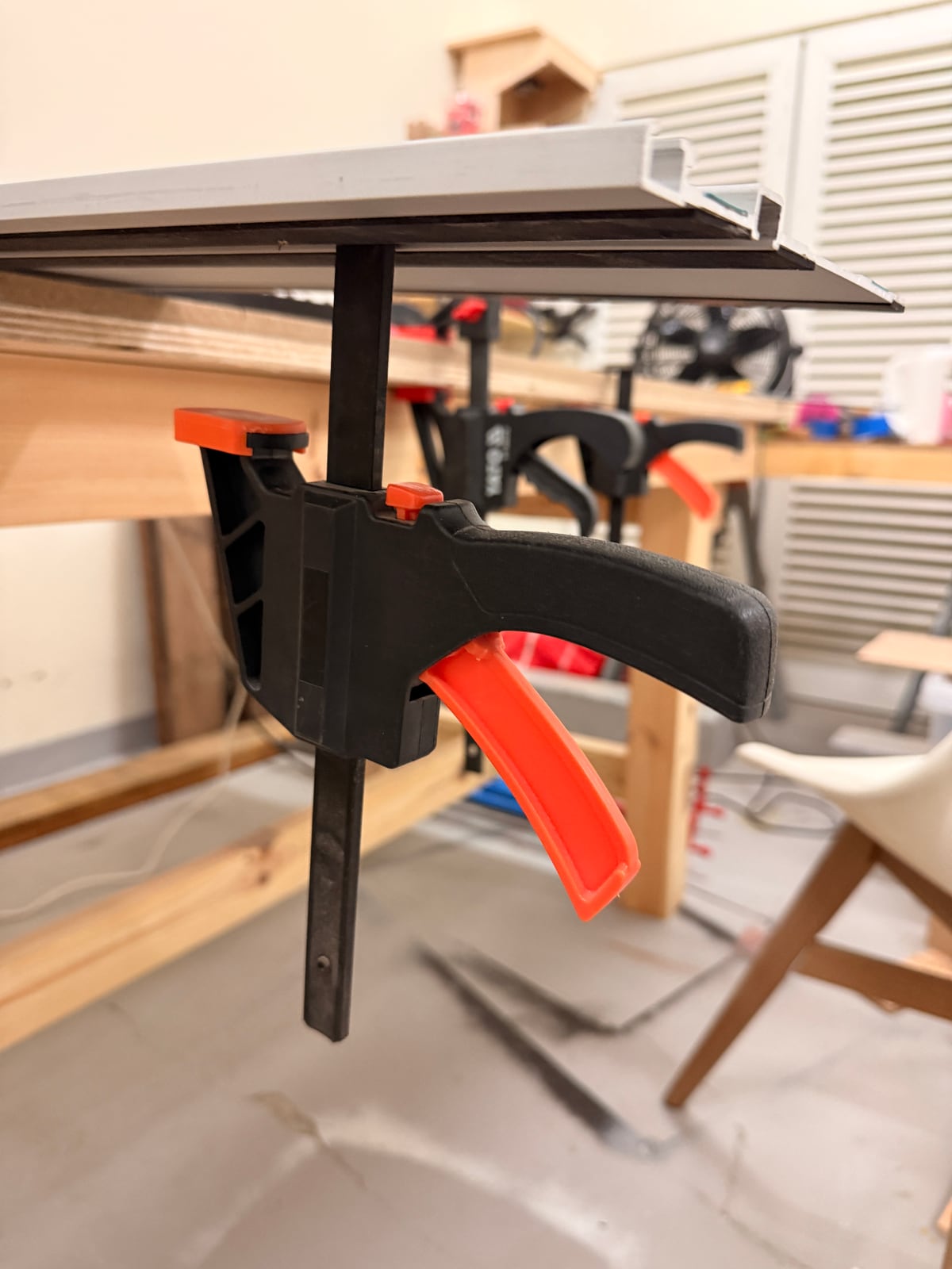 A quick-release clamp engaged in the T-slot on the underside of a guide rail, gripping the workpiece from beneath.