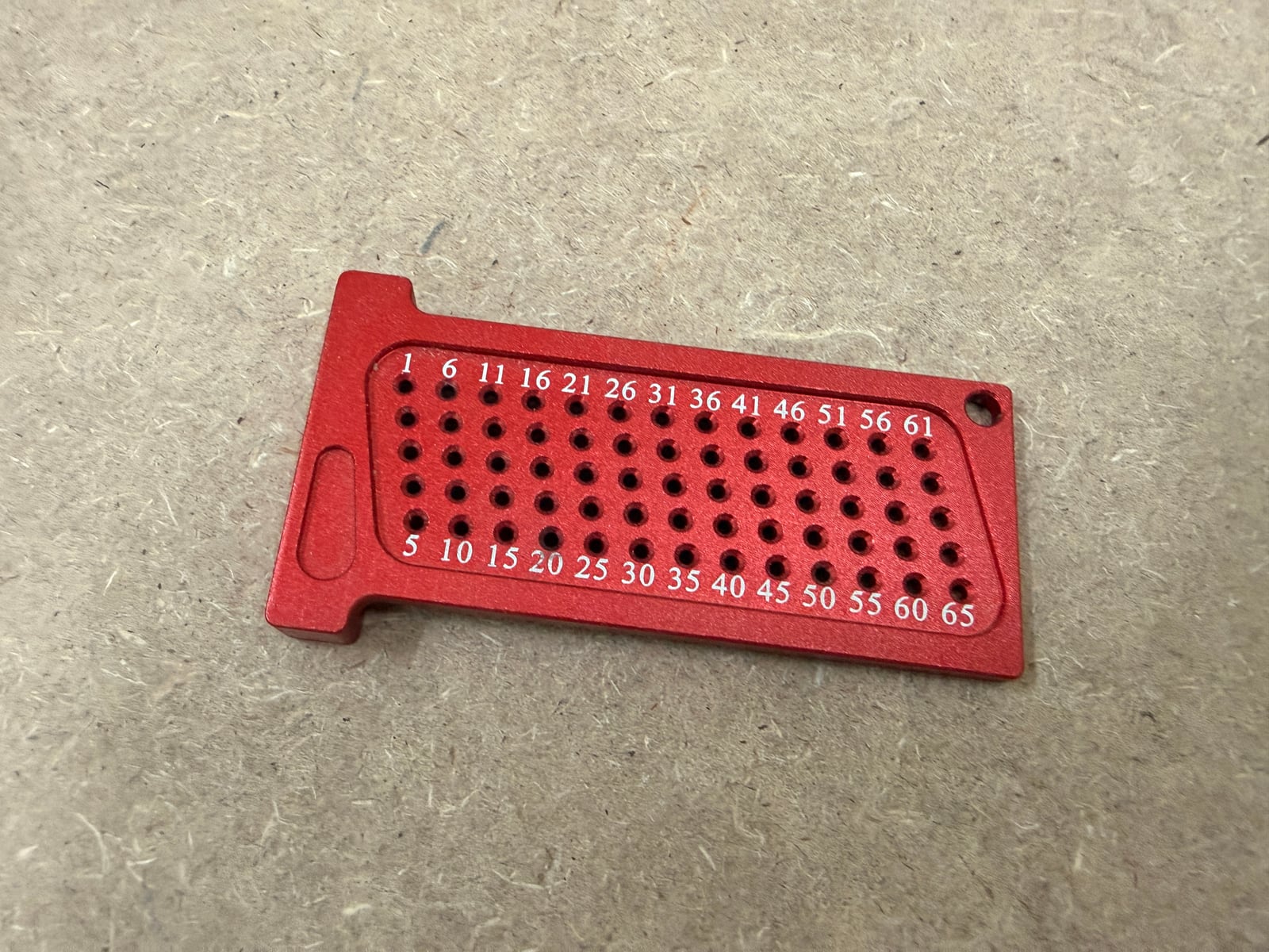 A marking ruler. The T-shaped end is the fence that rides the board edge; the holes are numbered 1 to 65, each one millimetre further out than the last.