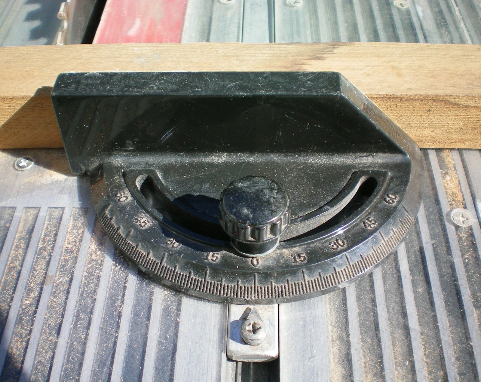 A miter gauge in a table saw slot, head swung off ninety degrees against its protractor scale.