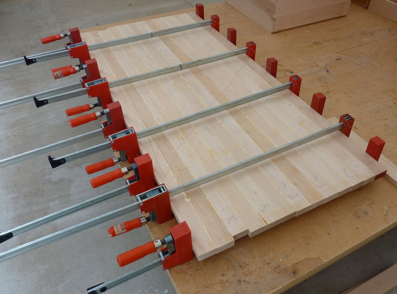 Parallel clamps closing a panel glue-up. The tall jaws stay square to the bar under load, which is what keeps the panel flat instead of bowing it.