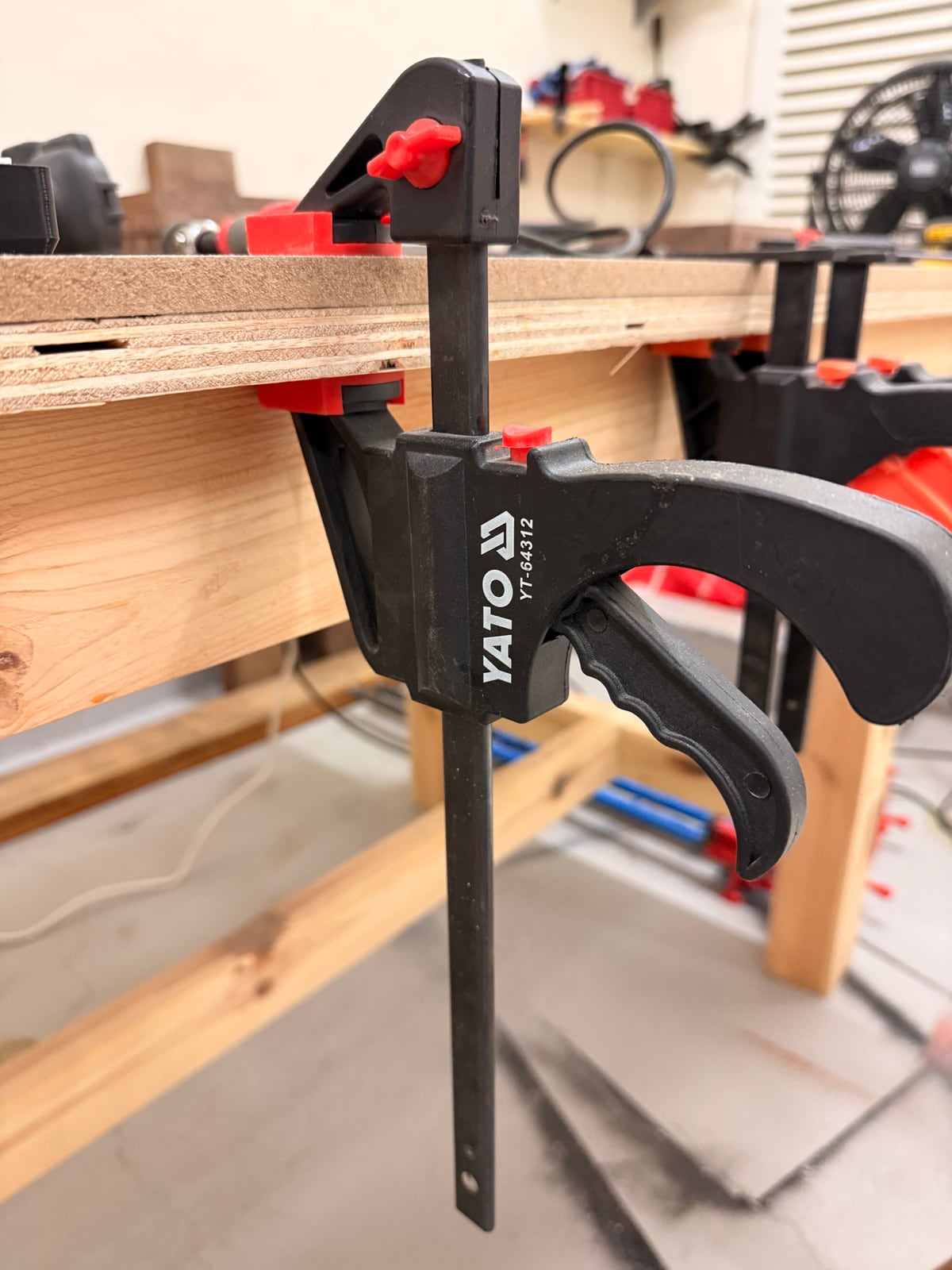 A one-handed trigger clamp on a bench top. The trigger drives the jaw closed, so the other hand stays free to hold the workpiece.