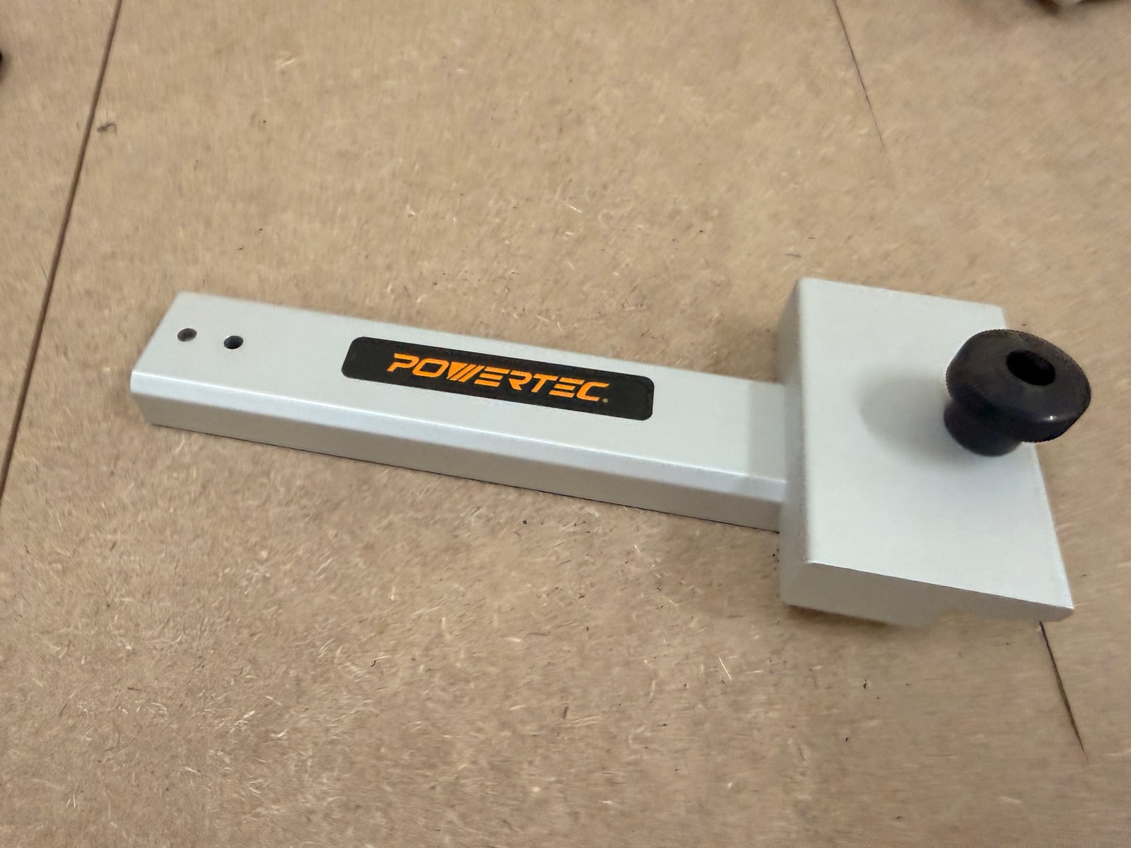 A track saw square, with the long arm registering against the guide rail and the head hooking over the edge of the sheet.