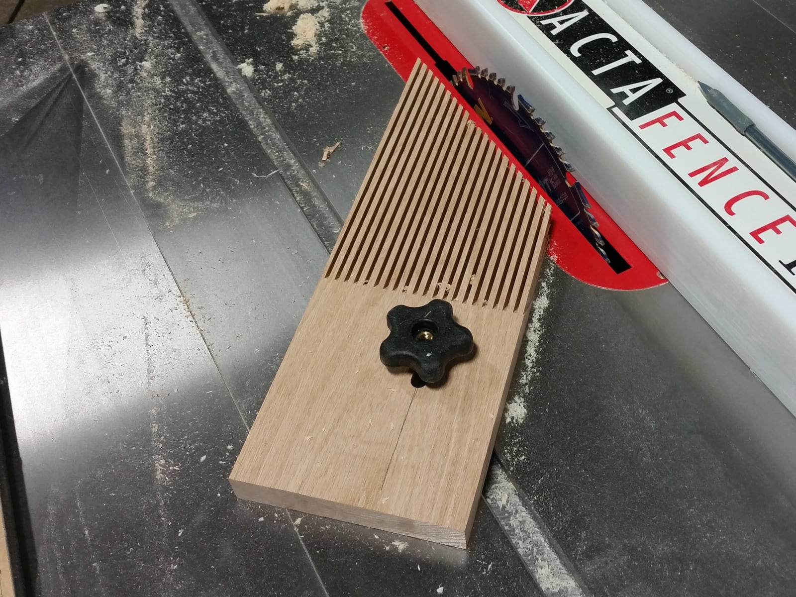 A featherboard clamped to a saw table, its angled fingers holding stock against the fence. They flex as the board feeds forward and resist it coming back.