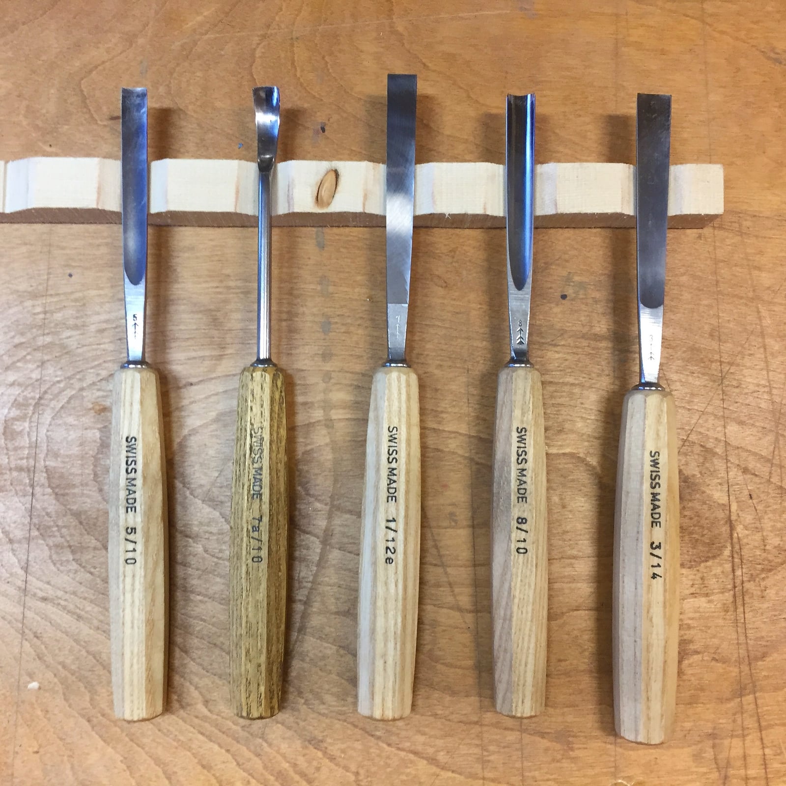 Carving gouges racked by size. Each carries its sweep -- how curved the cutting edge is -- alongside its width.