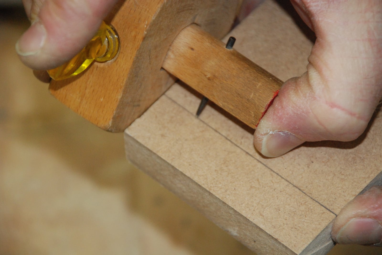 A marking gauge scoring a line. The fence rides the edge, the pin cuts the fibres rather than drawing on them, so the line stays put.