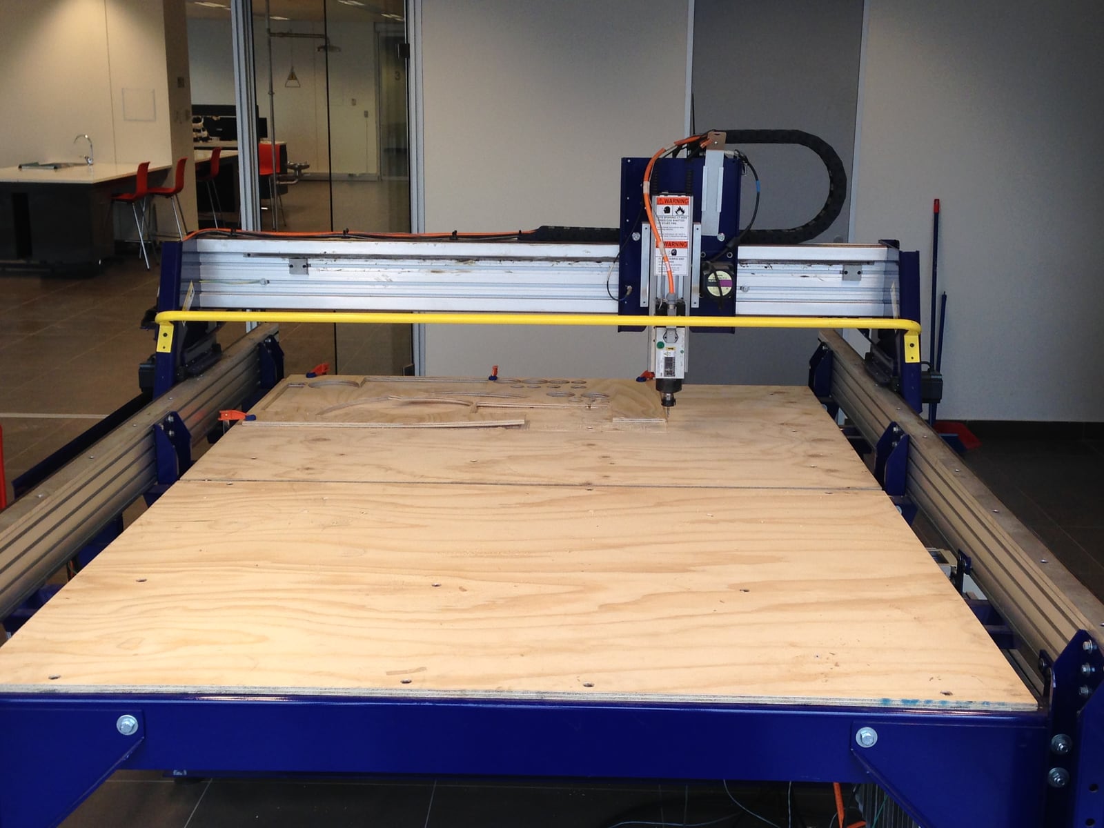 A CNC router: a spindle carried on a gantry over a flat bed, cutting a path from a file rather than from a fence.