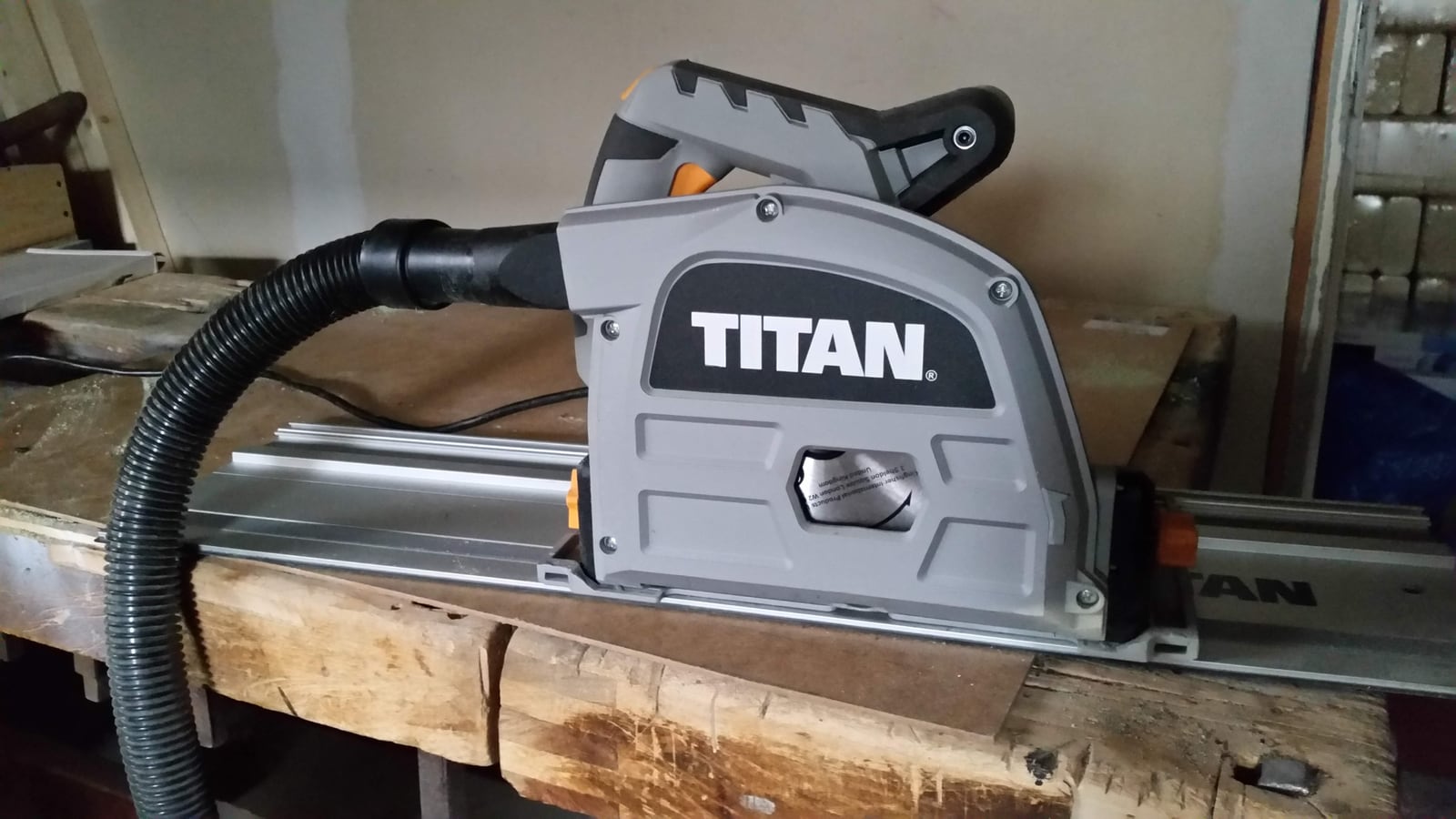 A track saw mounted on its guide rail, attached to a dust extraction system